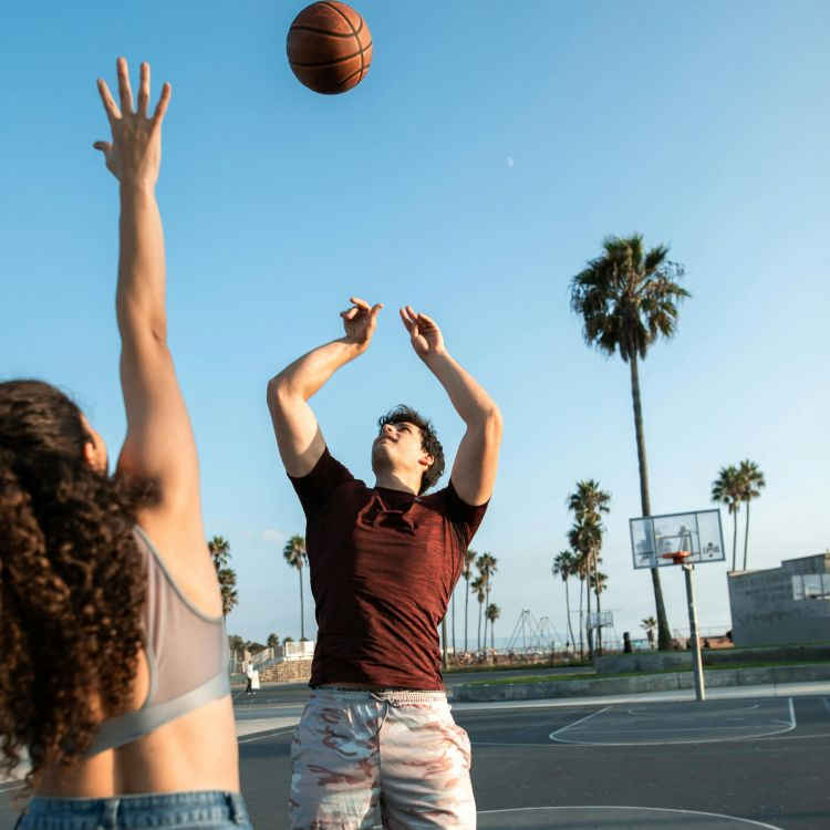 Two people playing basketball outdoors on a sunny day, symbolizing active lifestyle, movement, and sportswear.