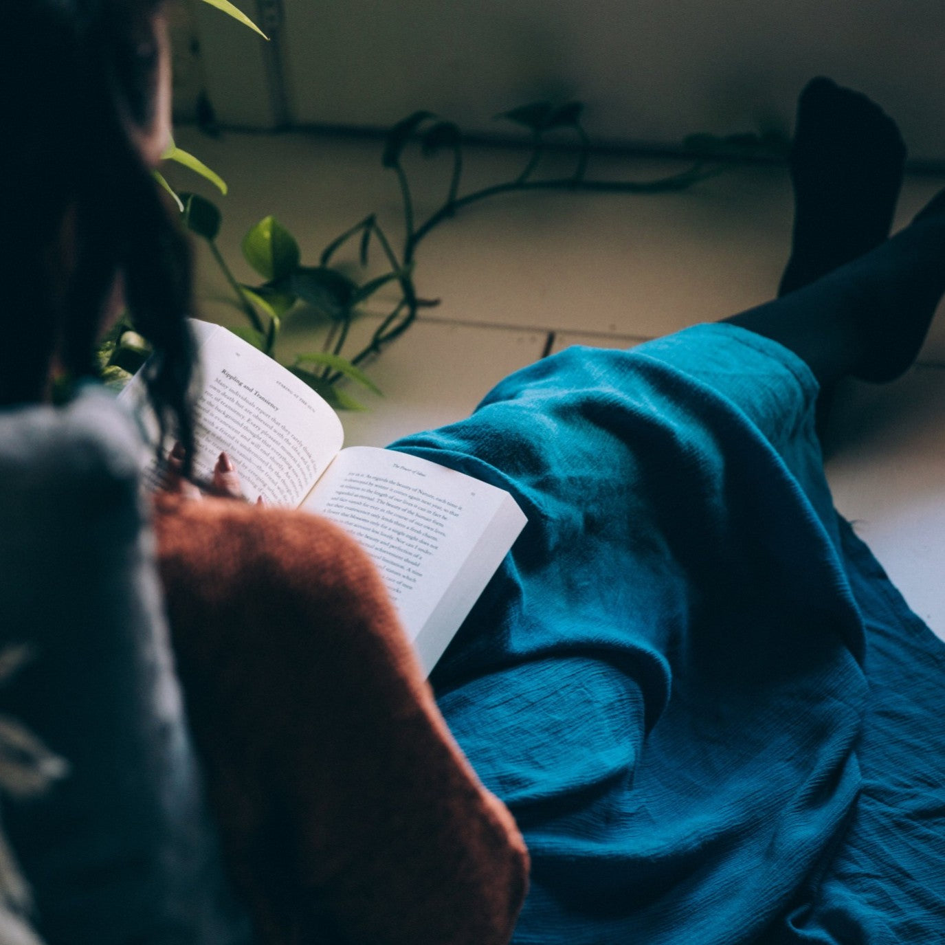 Woman relaxing at home, sitting on the floor and reading a book in cozy loungewear.