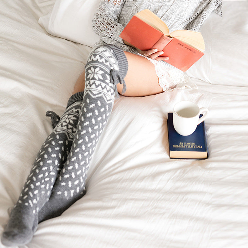 Person wearing patterned socks on a bed with a book and mug.