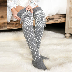Gray Nordic-pattern knee-high socks worn by a person sitting on a fluffy white rug.