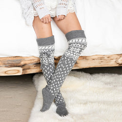 Person wearing gray patterned knee-high socks on a white surface