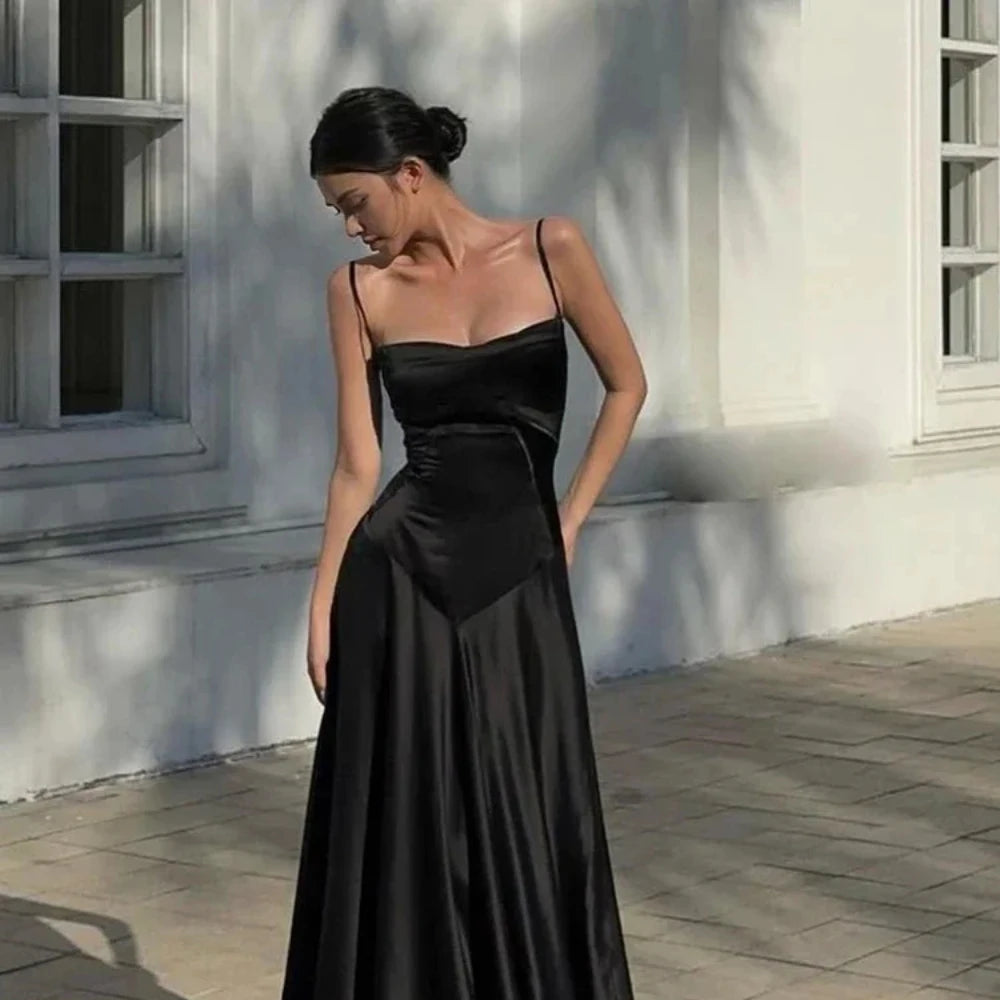 Woman in a black evening gown standing in front of a white wall.