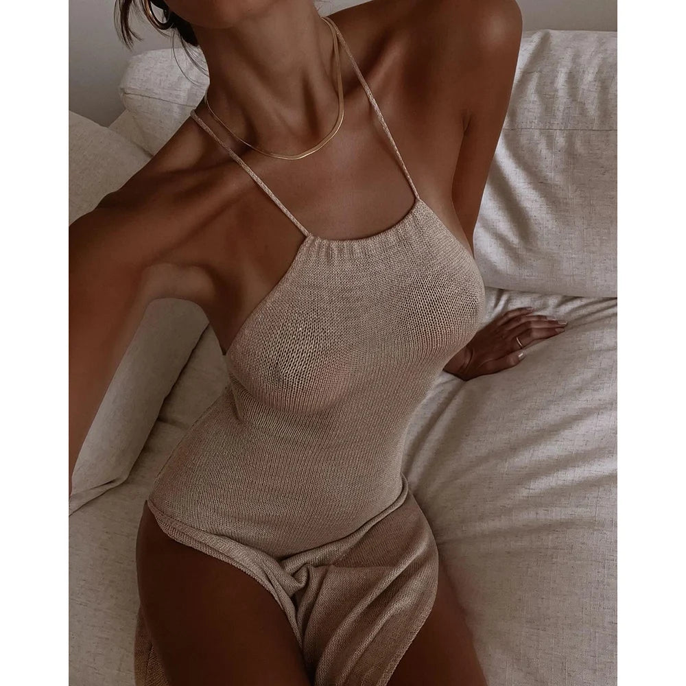Woman wearing a beige bodysuit sitting on a bed.