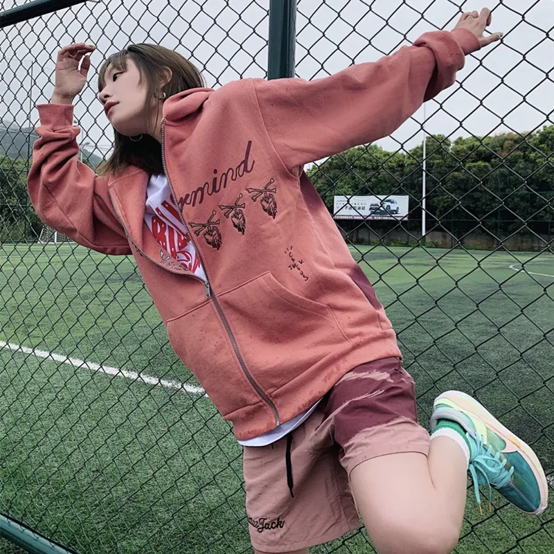 Person wearing a pink hoodie and shorts on a tennis court
