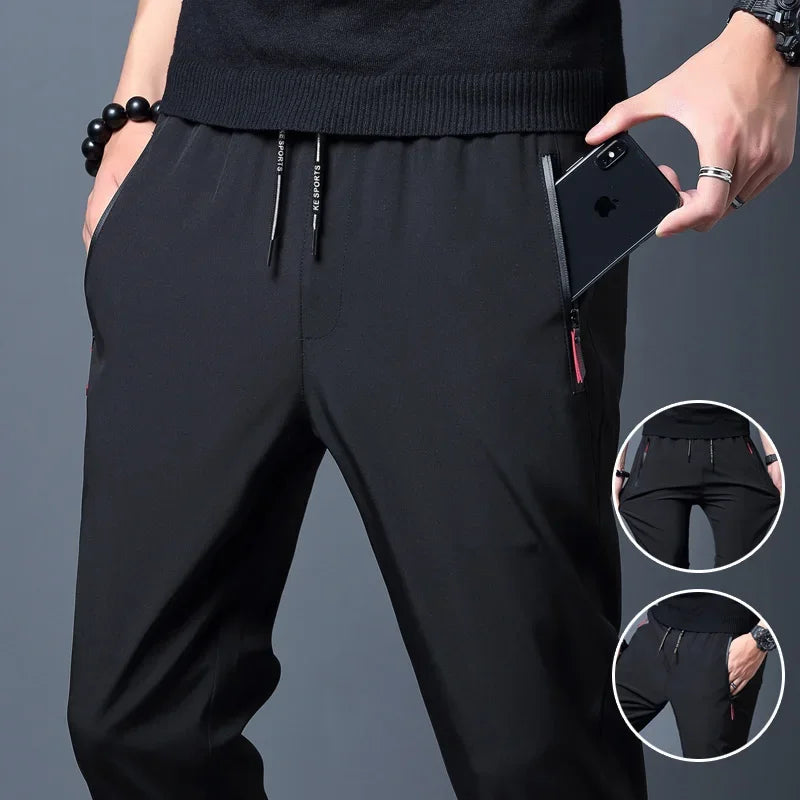 Men's slim fit black jogger pants with elastic waistband and a pair of hands holding a mobile phone in the pocket. Additional images show the pants' closure and detailed texture.
