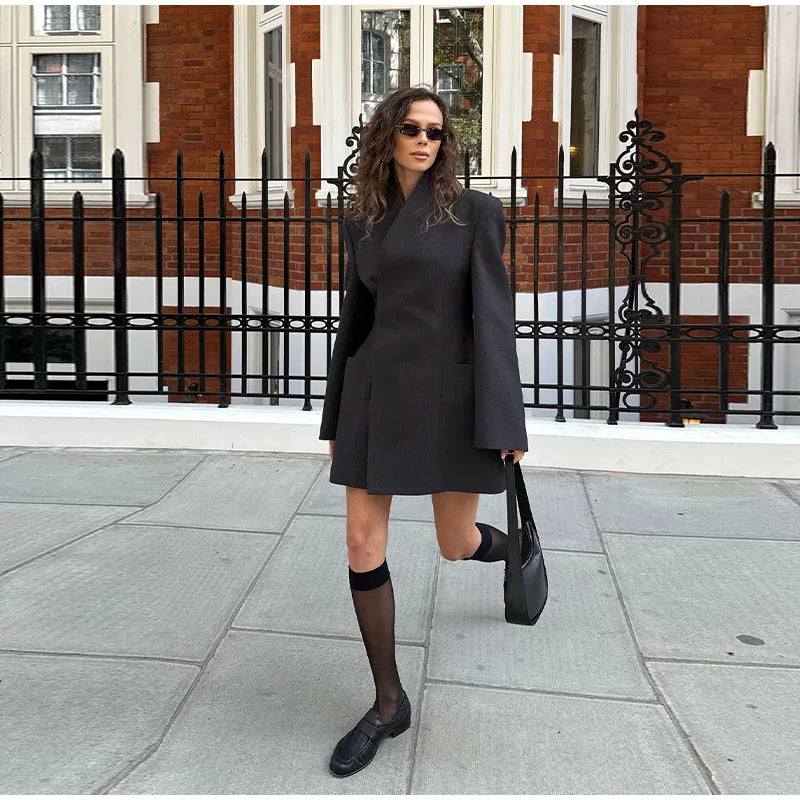 Woman in a black outfit standing on a sidewalk with a building in the background