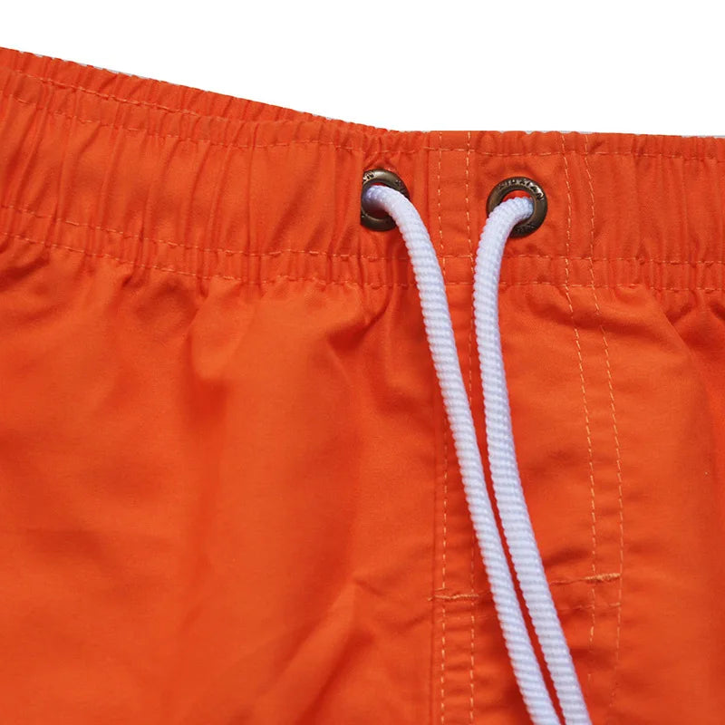 Close-up of orange swim shorts with a white drawstring on a white background