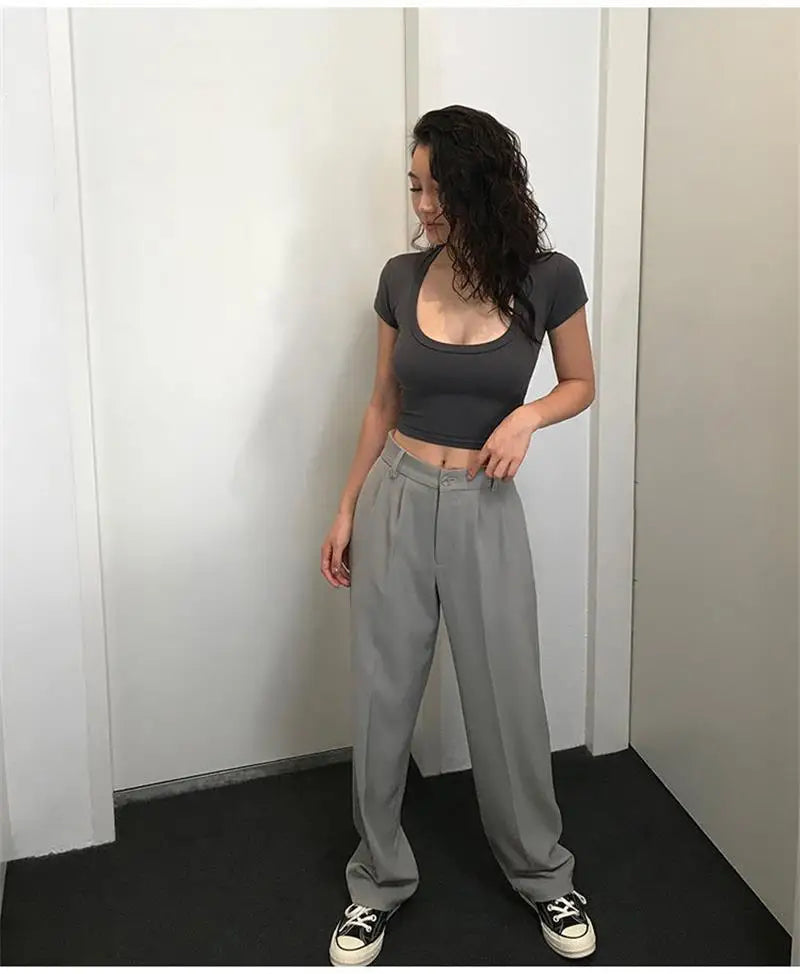 Person wearing a gray crop top and light gray pants standing against a white wall.
