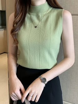A woman wearing a green knitted tank top with a turtleneck neckline and sleeveless design.