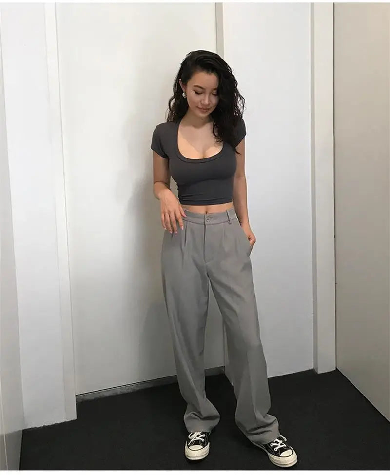 Woman wearing a crop top and wide-leg pants against a white wall.