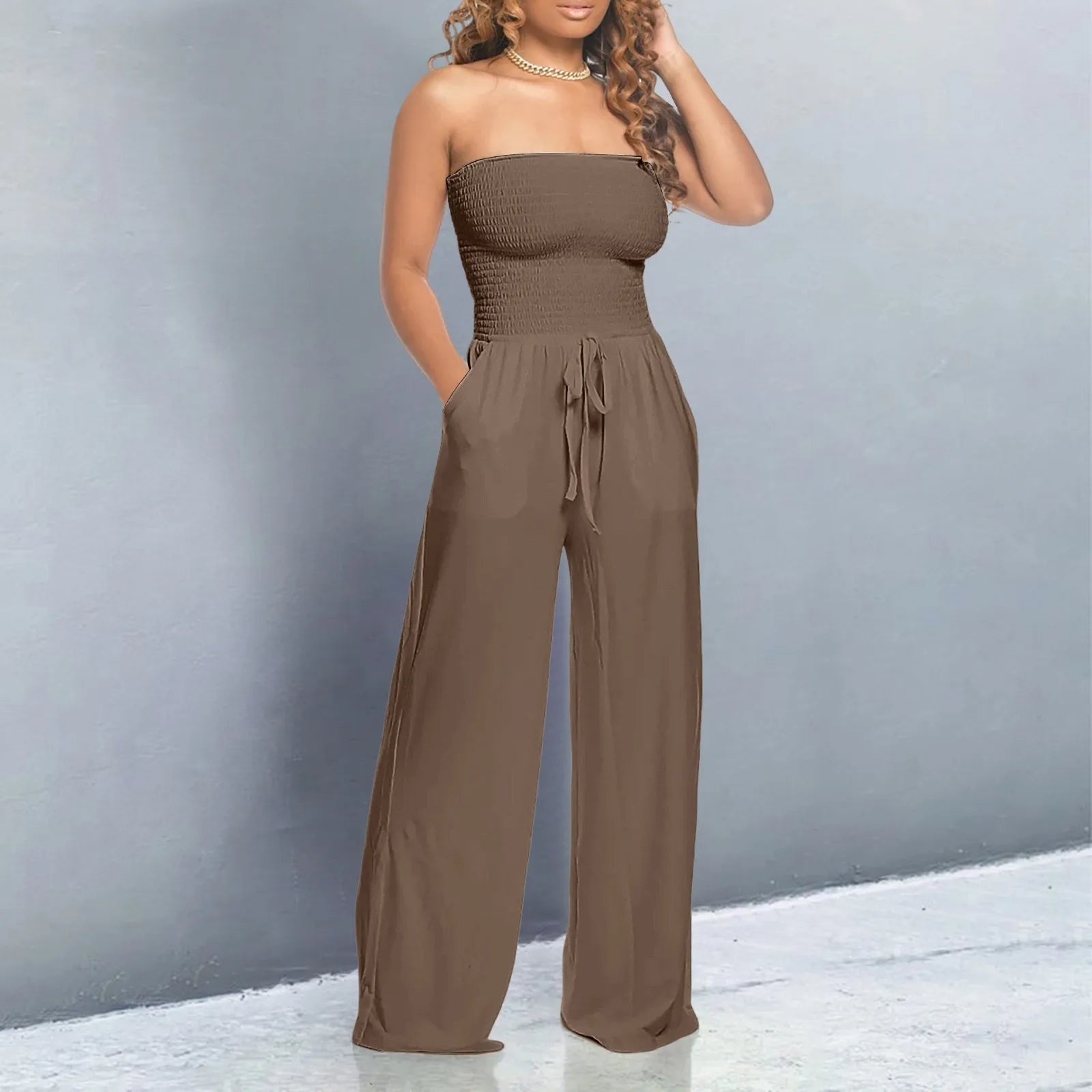 Woman wearing a brown strapless jumpsuit against a gray background