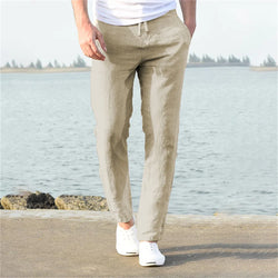 A pair of beige men's cotton linen pants worn by a model standing near a body of water, representing the casual style suitable for daily wear in spring and autumn.
