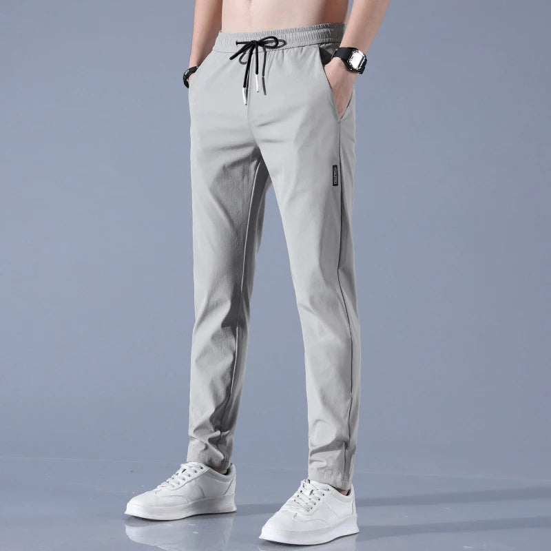 A pair of gray straight leg men's pants with an elastic waistband and drawstrings, featuring a mid-rise waist and a pencil pants style.