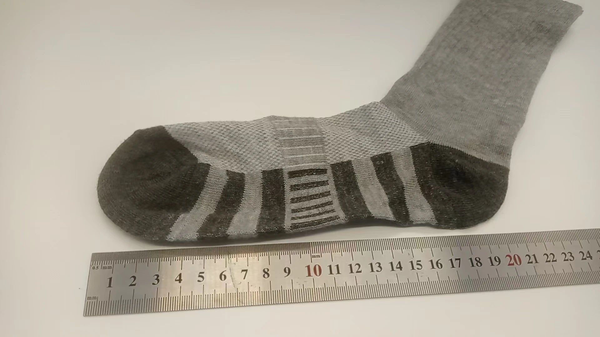 Gray sock with brown accents on a white surface next to a ruler for size reference.