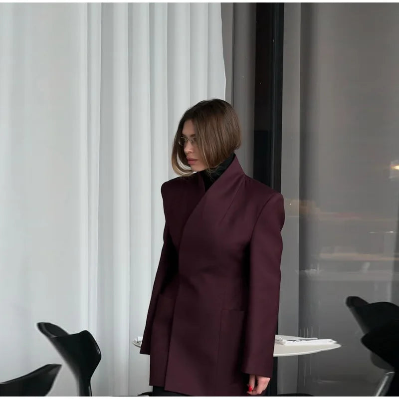Person wearing a burgundy coat standing in a room with white curtains and black chairs.