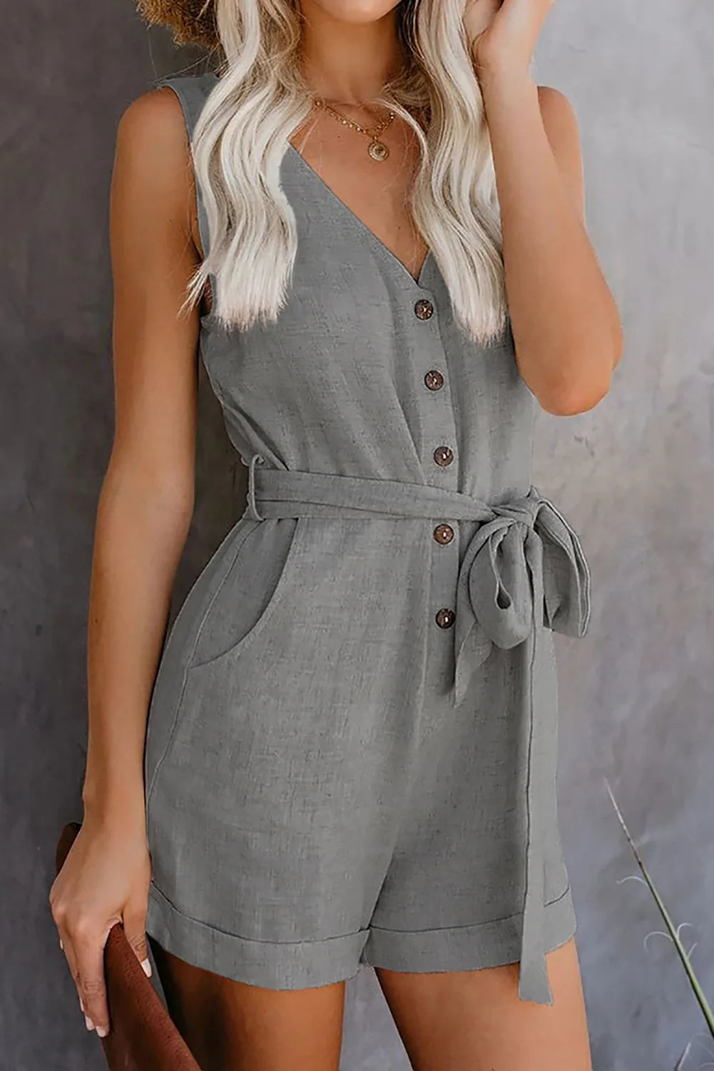 Woman wearing a gray romper with a belt against a neutral background