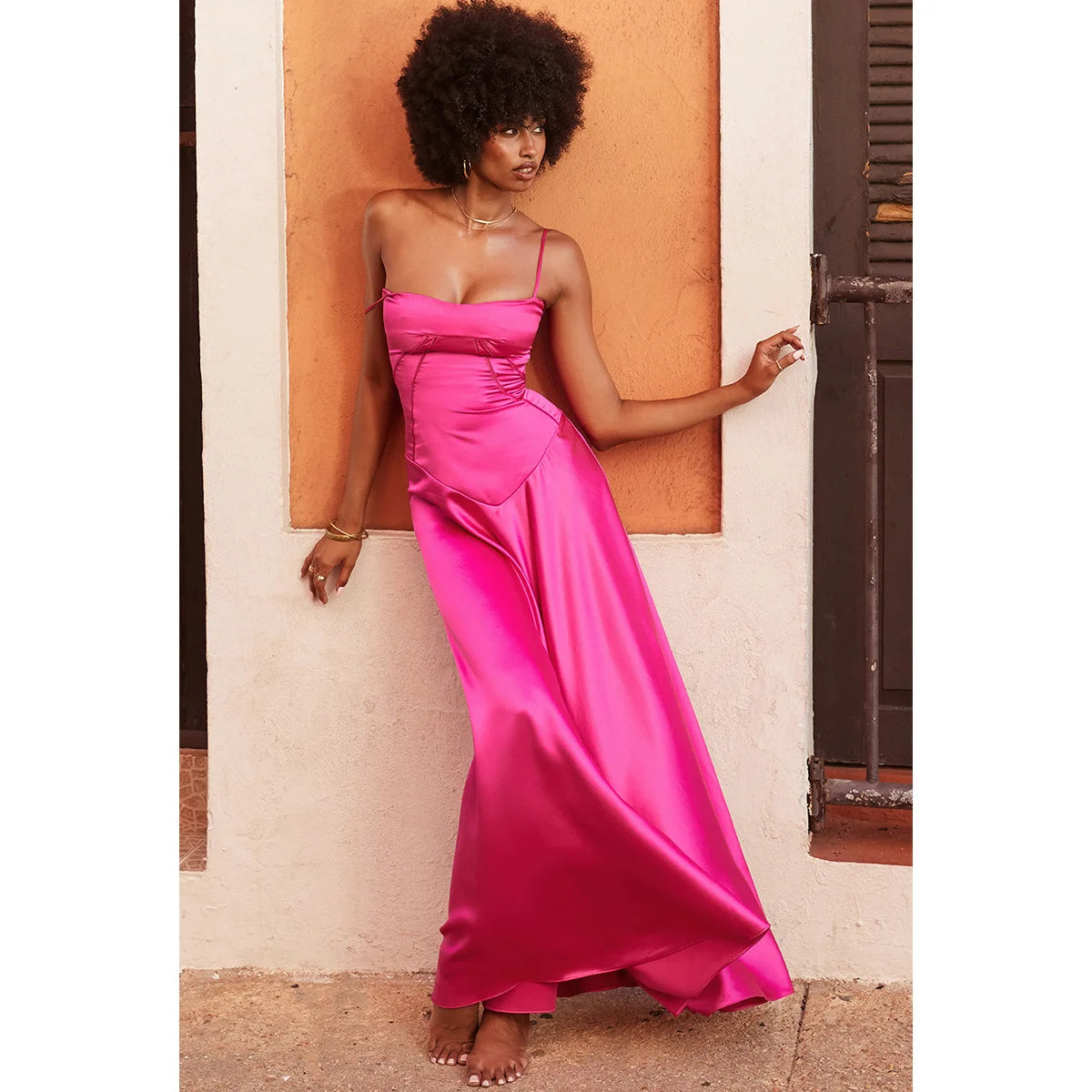 Woman in a pink dress standing against a wall.