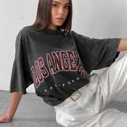 A woman modeling a black acid washed t-shirt with 'LOS ANGELES CALIFORNIA' printed on the front.