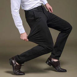 A man wearing a white shirt and black formal trousers with elastic straight fit, standing against a grey background.