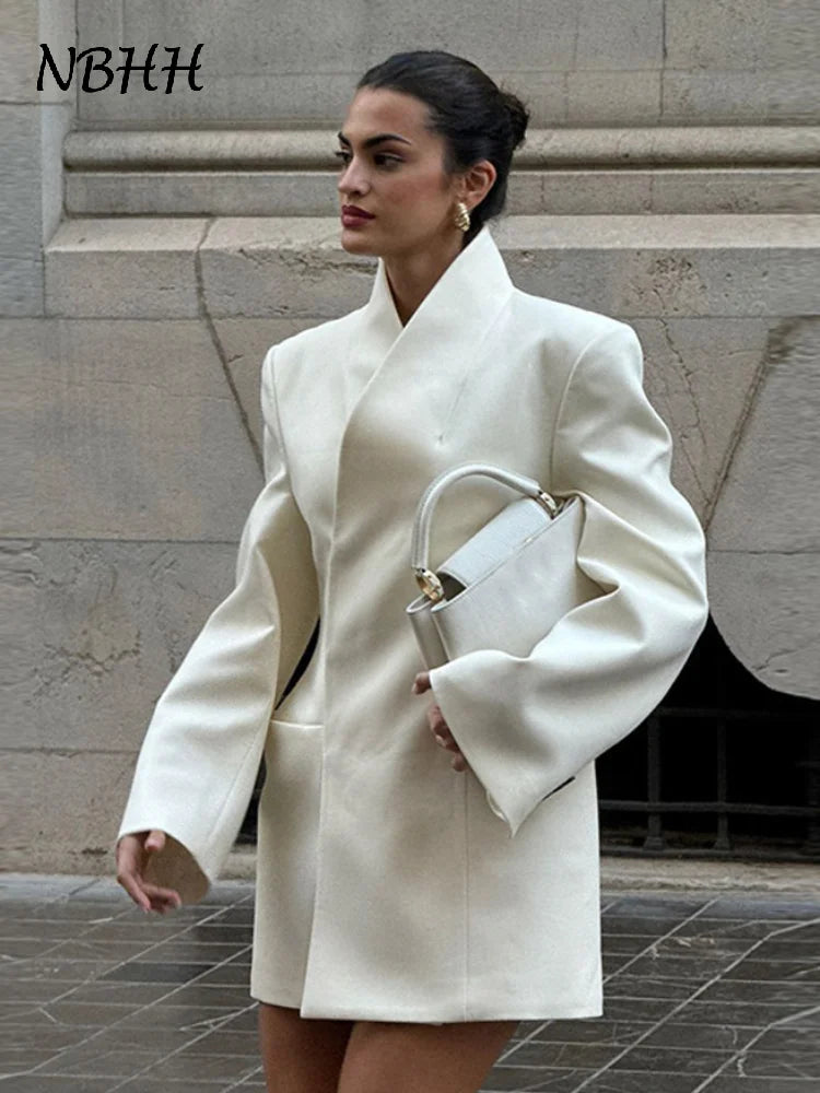 Woman in a white coat holding a handbag against a stone wall background