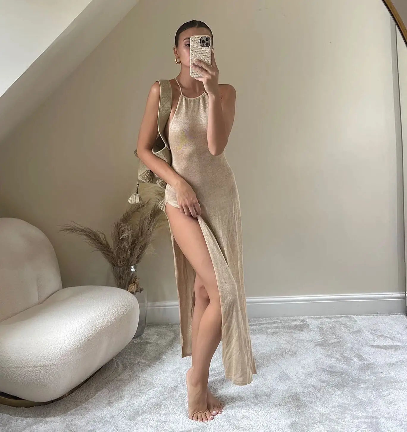 Woman in a beige dress standing in a room with a white couch and decorative plant.