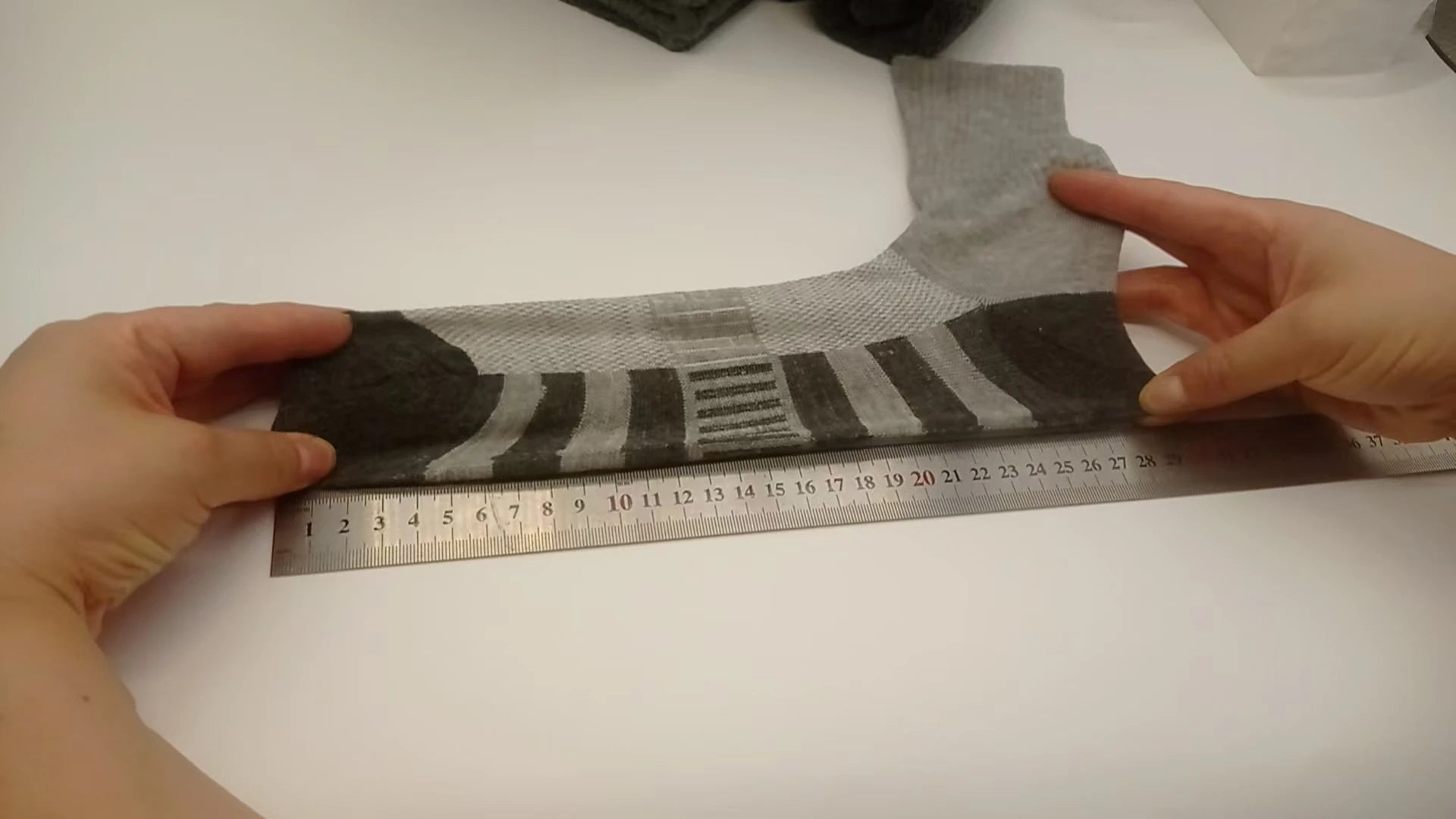 Gray sock with brown accents on a white surface next to a ruler for size reference.