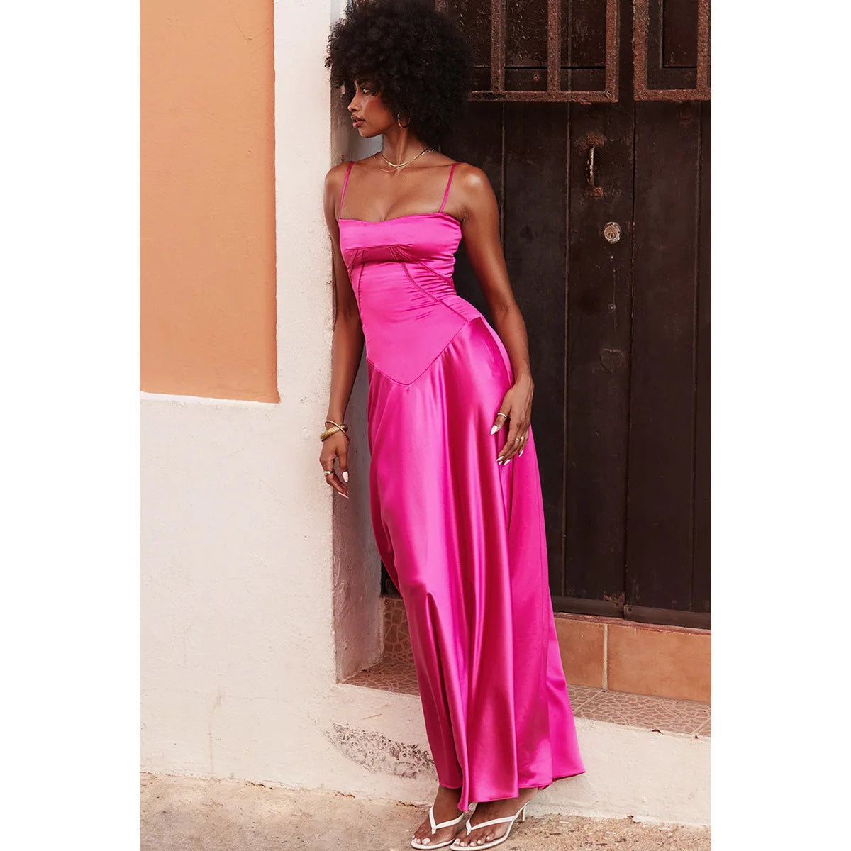 Woman in a pink dress standing against a wall.