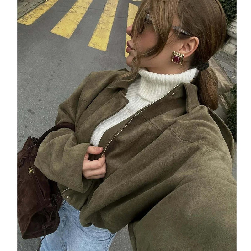 Person wearing a brown coat over a white turtleneck sweater on a street.