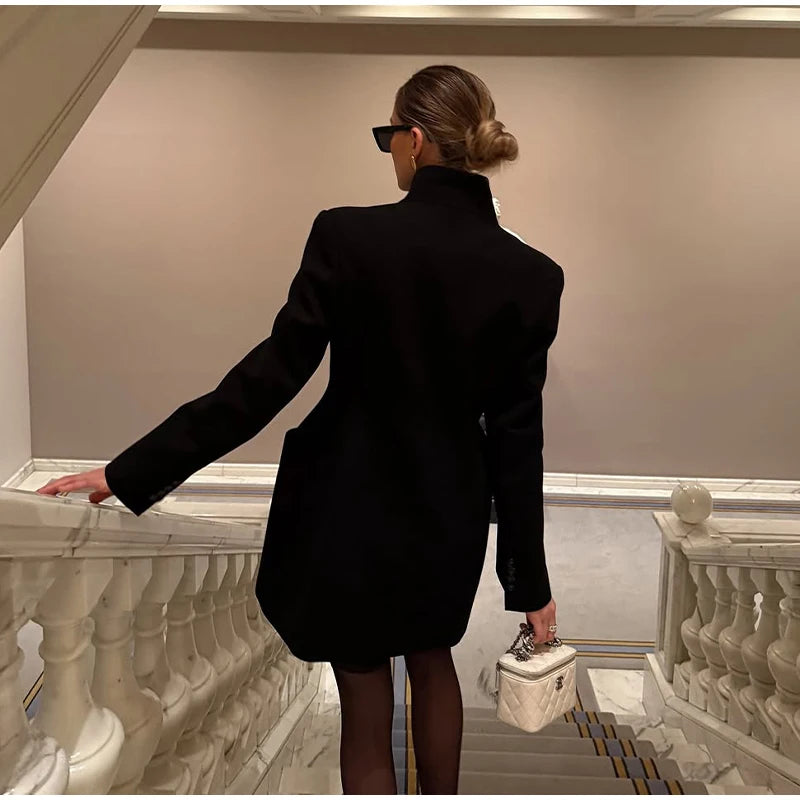 Woman in a black coat standing on a staircase holding a white handbag.