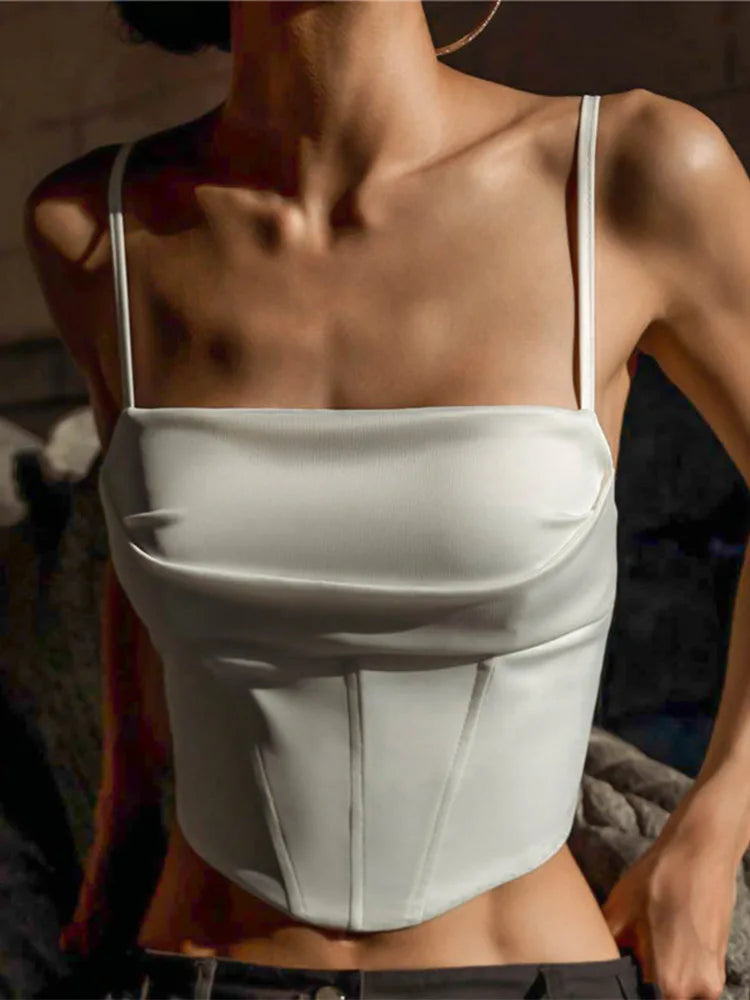A woman wearing a white spaghetti strap tank top with a backless design and bandage details.