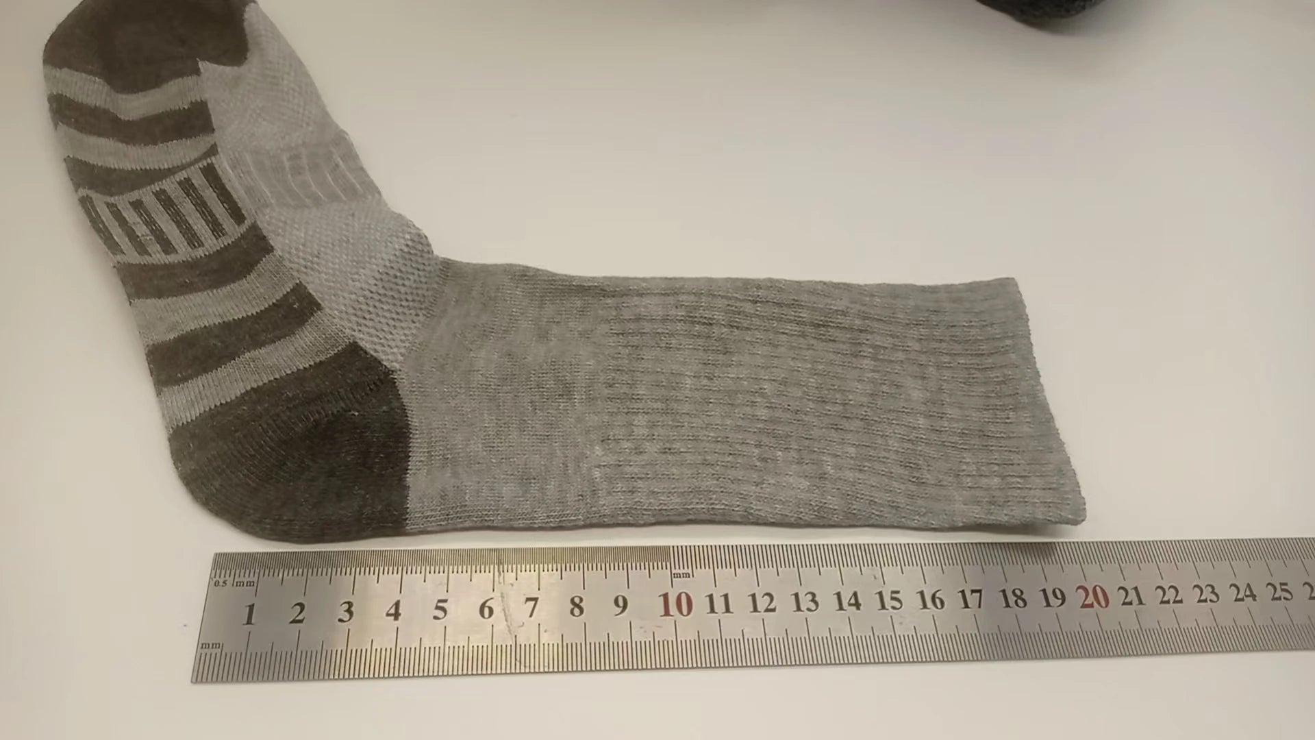 Gray sock with brown accents on a white surface next to a ruler for size reference.