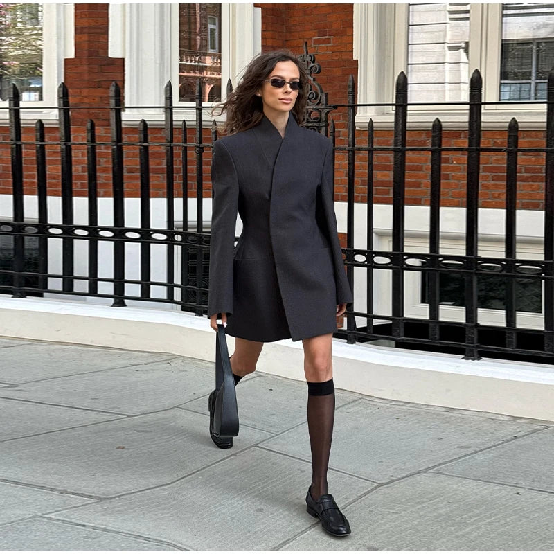 Woman in a black coat and sunglasses walking on a city street.