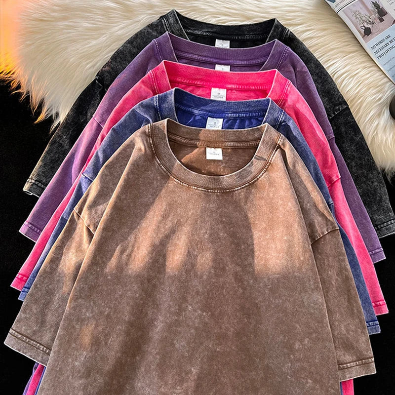 A stack of various colored washed vintage t-shirts, displaying colors such as brown, purple, blue, and pink, with a casual, streetwear vibe.