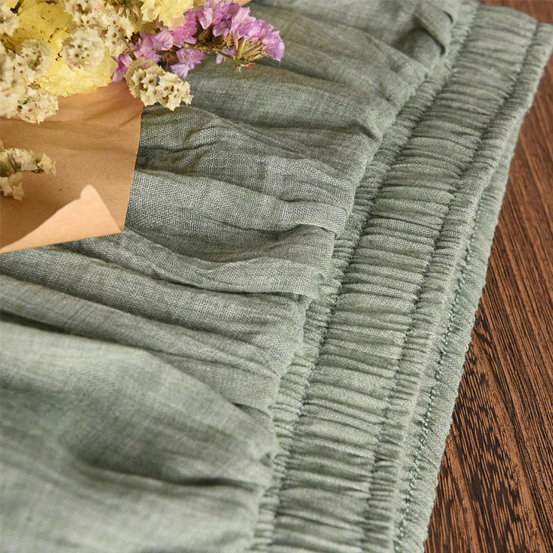 Close-up of a textured olive green fabric with a wooden surface and flowers in the background