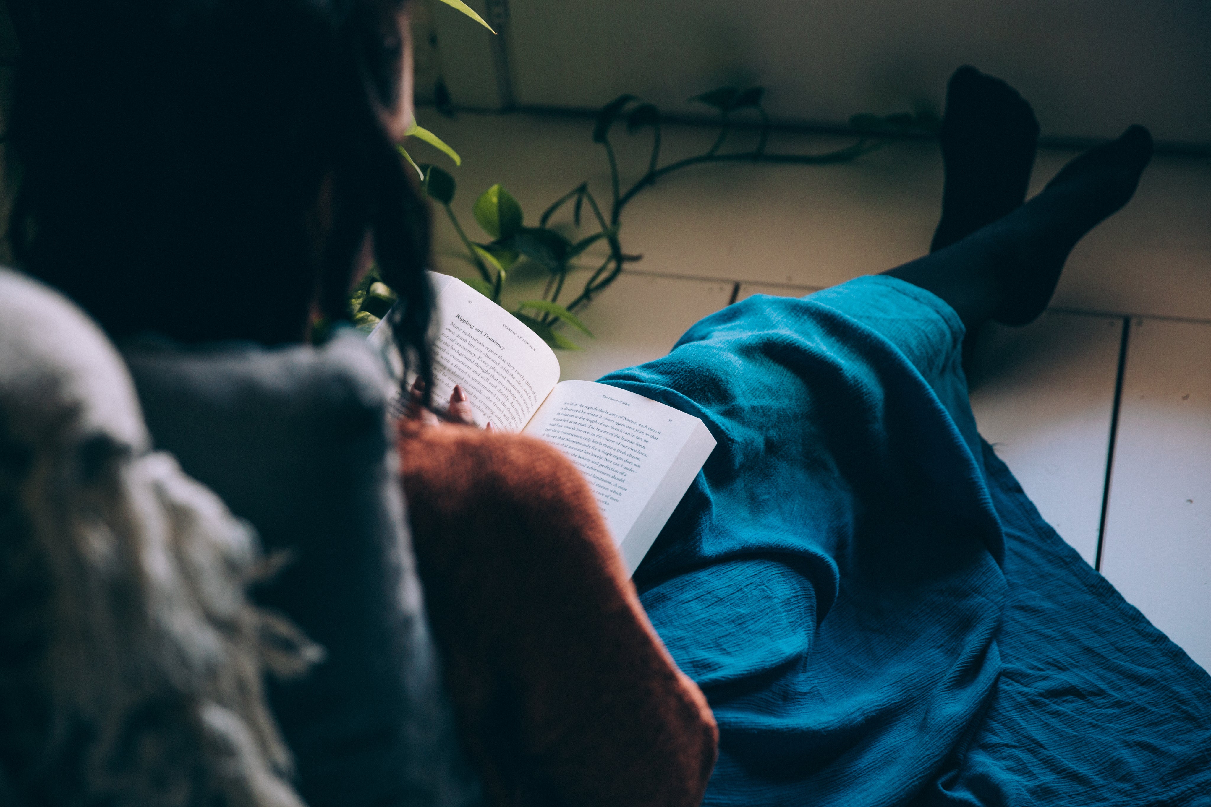 Woman relaxing at home, sitting on the floor and reading a book in cozy loungewear.